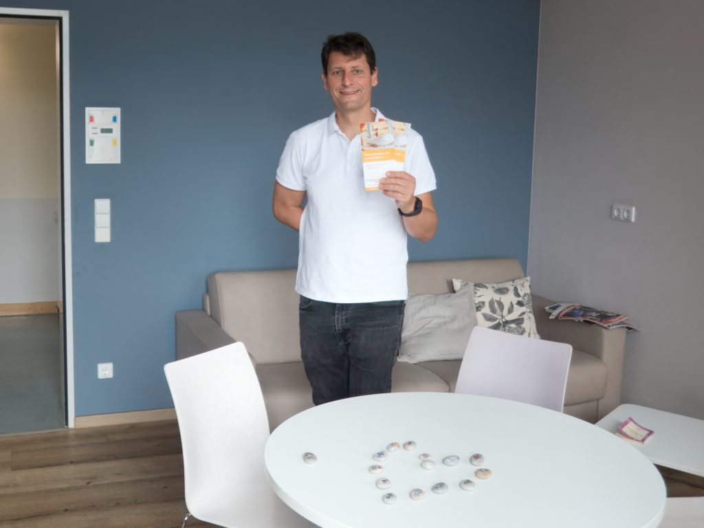 Jan steht im Elternzimmer mit einem Flyer  und bemalten Steinchen